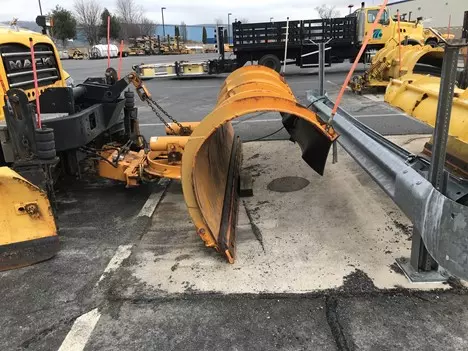 An image of a large curved yellow plow that is attached to a parked yellow PennDOT vehicle.